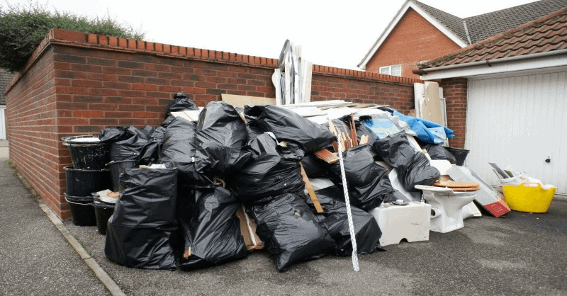 Piled garbage bags and discarded items near brick wall