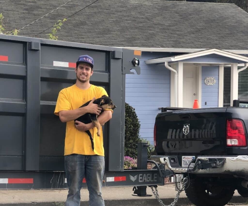 Man holding puppy in front of house and truck