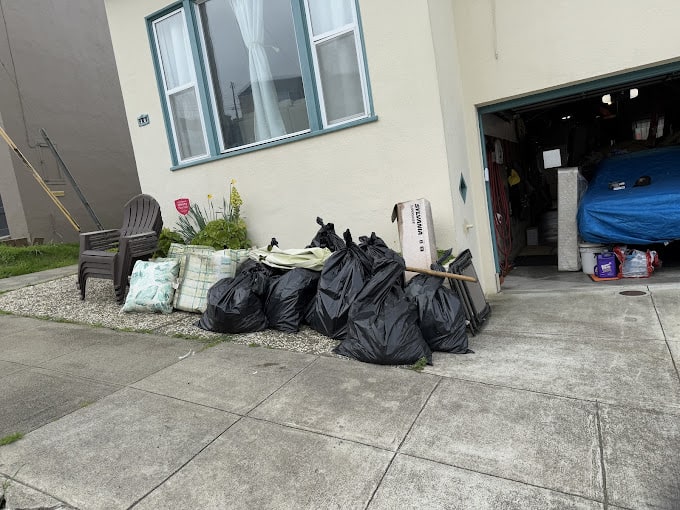 Garbage bags piled outside a house with open garage
