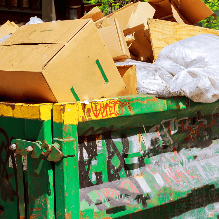 Overfilled dumpster with cardboard and graffiti