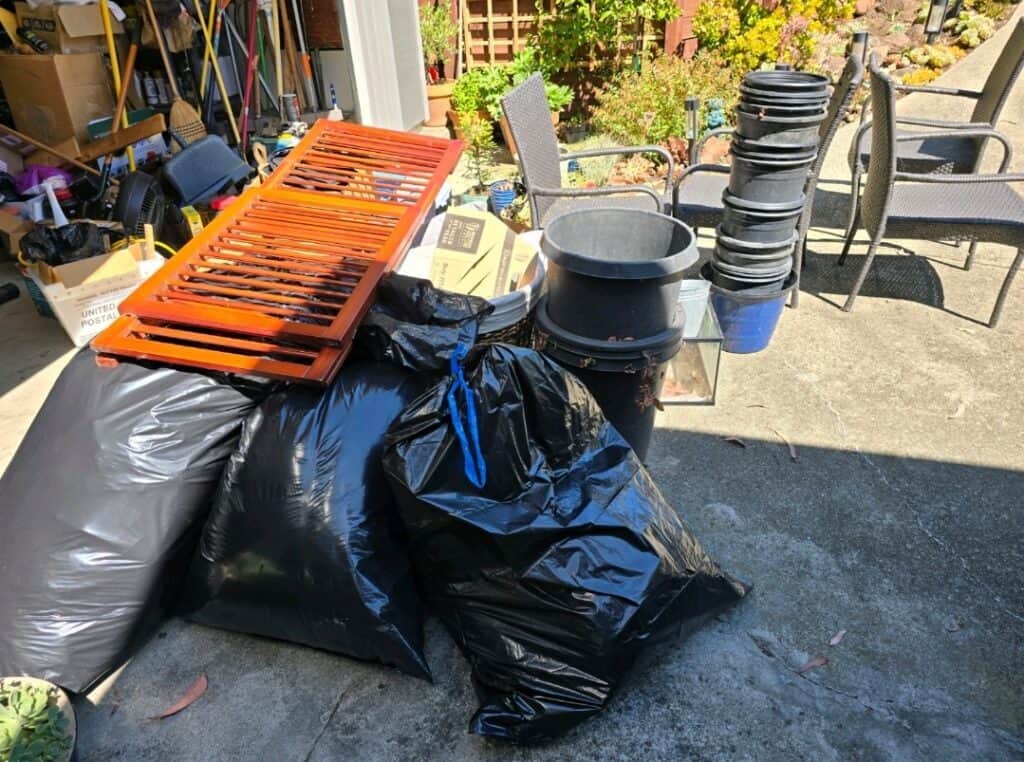 Cluttered garage with trash bags and various items outdoors