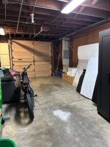 Cluttered garage with bike, mattress, and storage boxes.